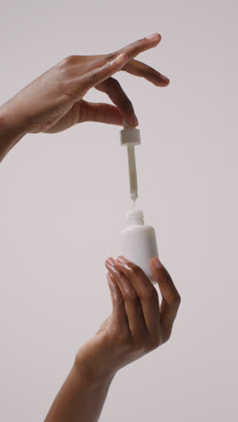 Close-Up-Of-Woman-Holding-Bottle-Of-Beauty-Product-And-Dropper-On-White-Background